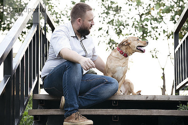 Mittlerer erwachsener Mann sitzt mit Hund auf einer Treppe im Freien