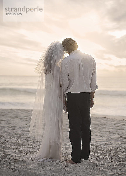 Neuvermähltes Paar steht am Strand bei Sonnenuntergang