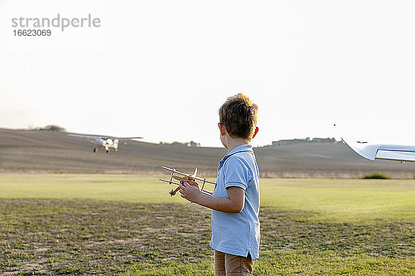 Kleiner Junge  der ein Spielzeugflugzeug hält  während er auf einem Flugplatz steht