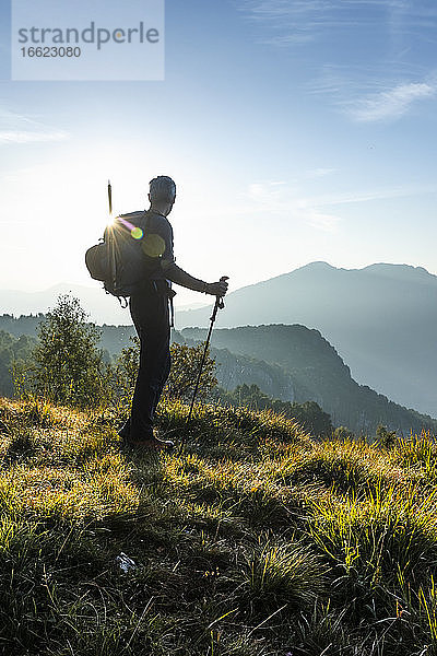 Silhouette eines männlichen Wanderers  der während des Sonnenaufgangs auf einem Berg steht und die Aussicht betrachtet  Orobie  Lecco  Italien