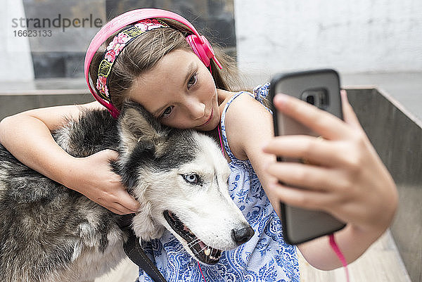 Mädchen mit Kopfhörer nimmt Selfie mit Hund zu Hause