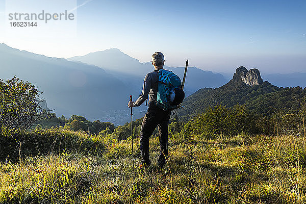Männlicher Wanderer mit Rucksack  der bei Sonnenaufgang den Berg gegen den Himmel betrachtet  Orobie  Lecco  Italien