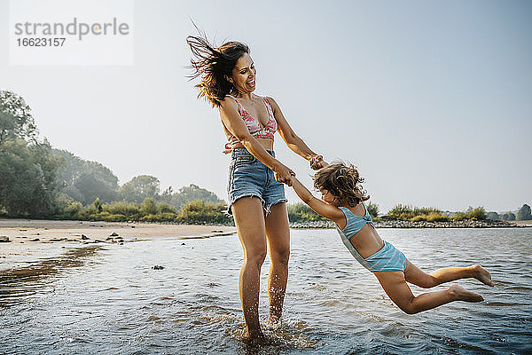 Mutter wirbelt Tochter herum  während sie am Strand im Wasser steht