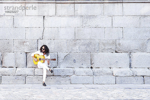 Gitarrist spielt Gitarre  während er an einer Betonwand sitzt