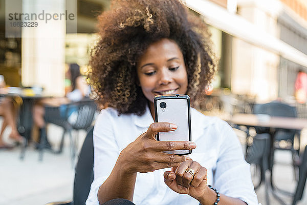 Frau  die ein Selfie mit ihrem Smartphone macht  während sie in einem Straßencafé sitzt
