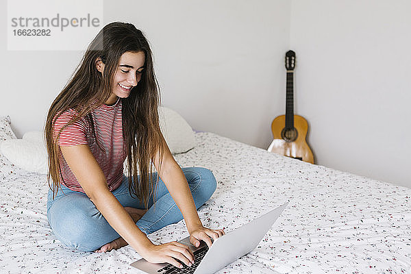 Junge Frau benutzt einen Laptop  während sie zu Hause im Schlafzimmer sitzt