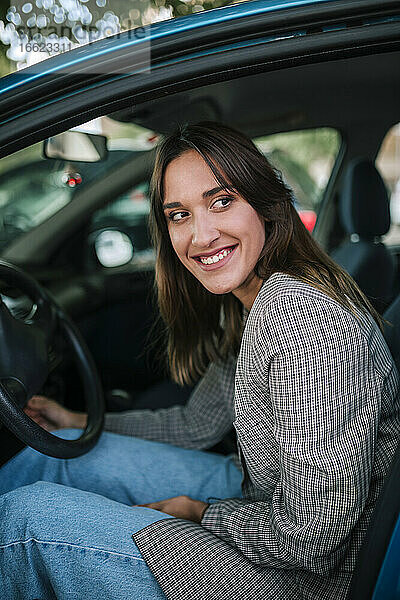 Lächelnde junge Frau  die im Auto sitzend nach draußen schaut