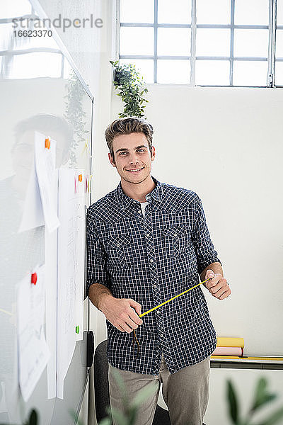 Lächelnder Mann  der sich im Büro an ein Whiteboard lehnt