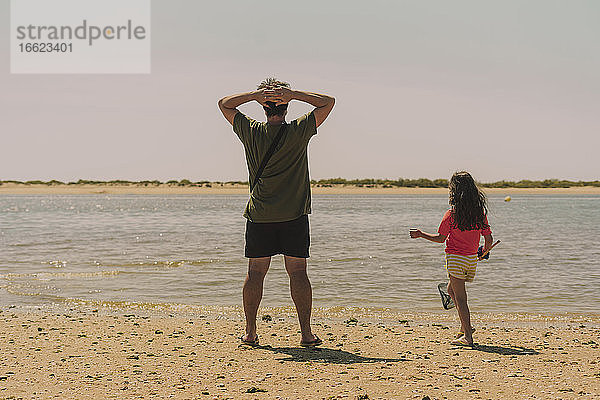Vater mit Tochter stehen am Strand gegen den klaren Himmel an einem sonnigen Tag