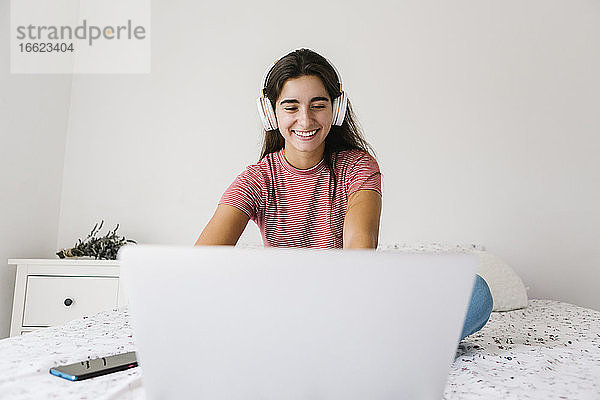 Junge Frau hört Musik  während sie zu Hause am Laptop arbeitet