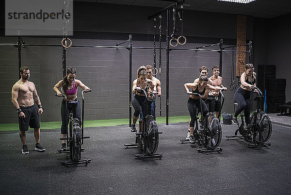 Frauen  die auf einem Fitnessrad trainieren  während Männer im Fitnessstudio dahinter stehen