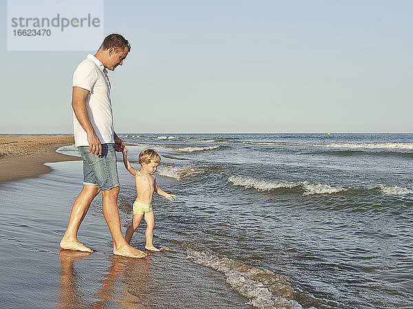 Junge hält die Hand seines Vaters beim Spaziergang am Strand