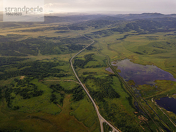Russland  Primorsky Krai  Zarubino  Luftaufnahme einer Straße  die sich in der Abenddämmerung entlang einer grünen Hügellandschaft erstreckt