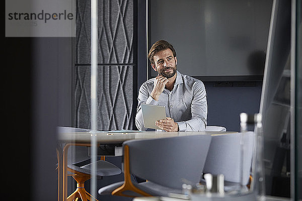 Nachdenklicher Geschäftsmann hält digitale Tabelle  während er im Büro sitzt
