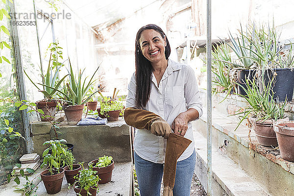 Lächelnde reife Frau  die einen Gartenhandschuh trägt  während sie im Gartenschuppen steht