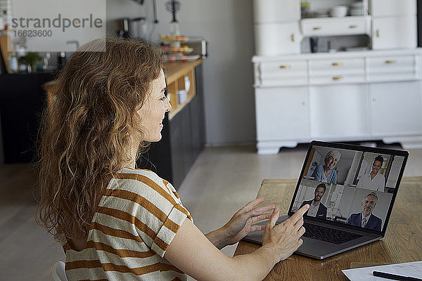 Frau  die zu Hause sitzend eine Videokonferenz über ihren Laptop abhält