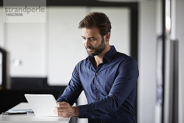 Geschäftsmann  der ein digitales Tablet benutzt  während er am Schreibtisch im Büro steht