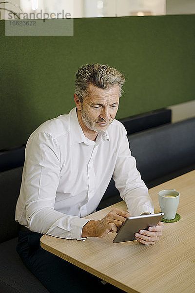 Mann  der ein digitales Tablet benutzt  während er am Tisch in der Cafeteria im Büro sitzt