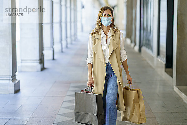 Frau mit Gesichtsmaske  die eine Tasche trägt  während sie in der Lobby eines Geschäfts in der Stadt spazieren geht
