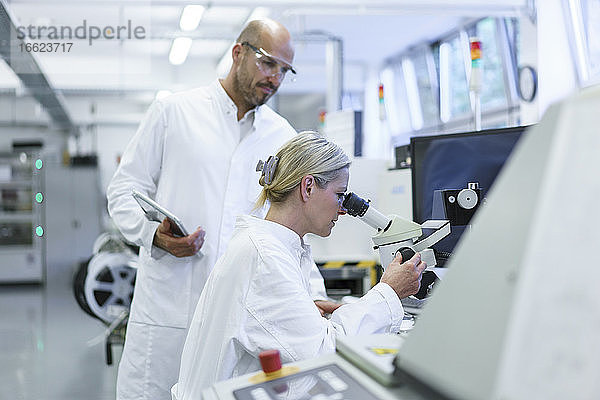 Männlicher Techniker steht neben einer Wissenschaftlerin  die in ein Mikroskop schaut  während sie im Labor forscht