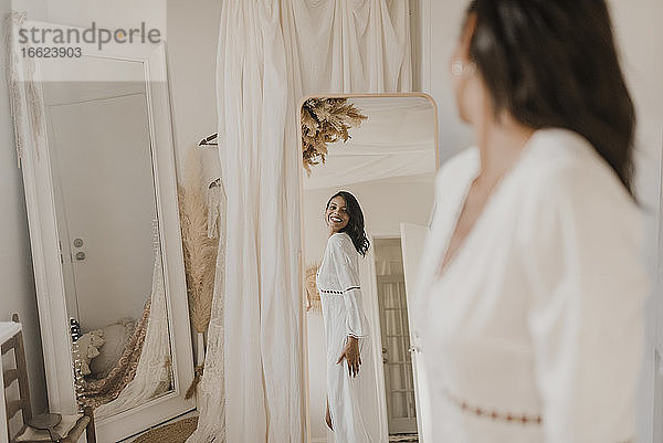 Junge Braut schaut in den Spiegel  während sie zu Hause steht
