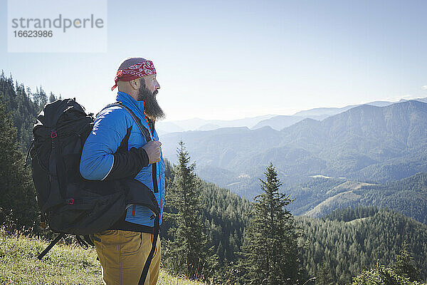 Bärtiger Mann mit Rucksack  der die Aussicht betrachtet  während er auf einem Berg gegen den klaren Himmel steht  Otscher  Österreich
