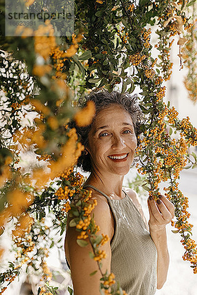Reife Frau berührt Orangenbaum an einem sonnigen Tag