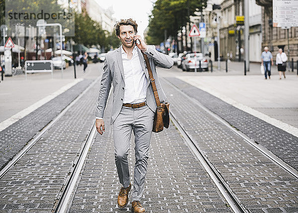 Lächelnder Mann  der mit seinem Handy telefoniert  während er in einer Straßenbahn in der Stadt spazieren geht