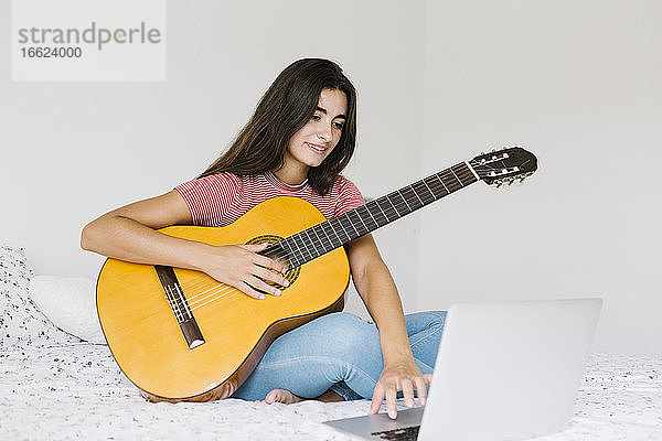 Frau lernt online zu Hause im Schlafzimmer Gitarre