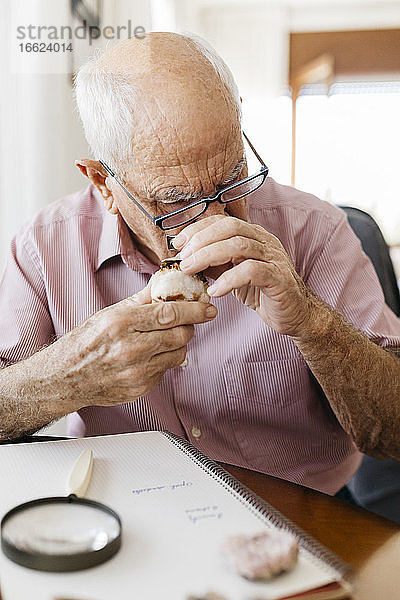 Älterer Mann betrachtet Mineral durch eine Lupe