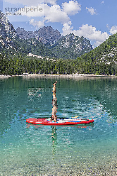 Mann macht Kopfstand auf dem Paddleboard am Pragser Wildsee vor der Bergkette  Dolomiten  Südtirol  Italien