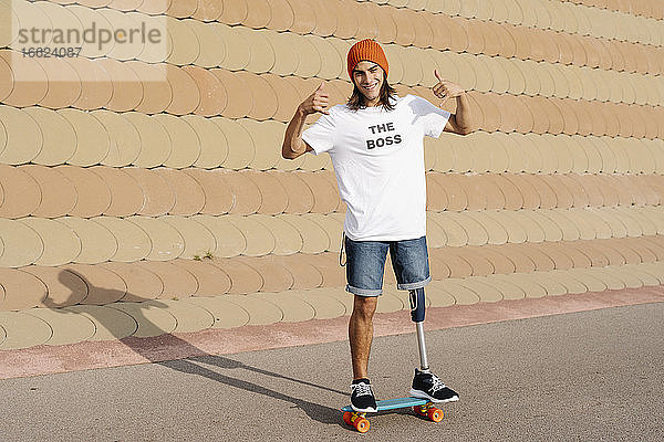 Junger behinderter Mann steht auf einem Skateboard auf dem Sportplatz