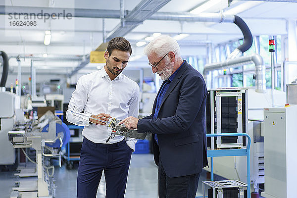 Ein leitender Angestellter zeigt auf ein Maschinenteil  während er mit einem Ingenieur an einer Maschine in einer Fabrik diskutiert