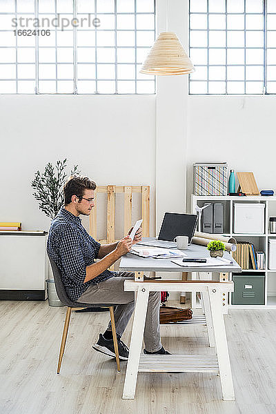 Architekt  der im Büro sitzend an einem digitalen Tablet arbeitet
