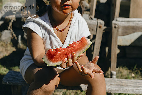 Mädchen isst Wassermelone und sitzt auf einem Baumstamm