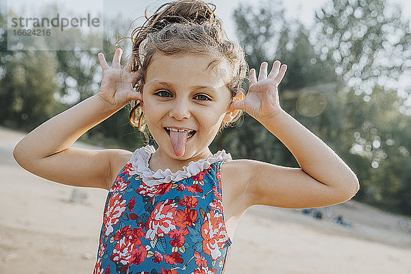 Niedliches kleines Mädchen streckt die Zunge heraus  während es am Strand steht