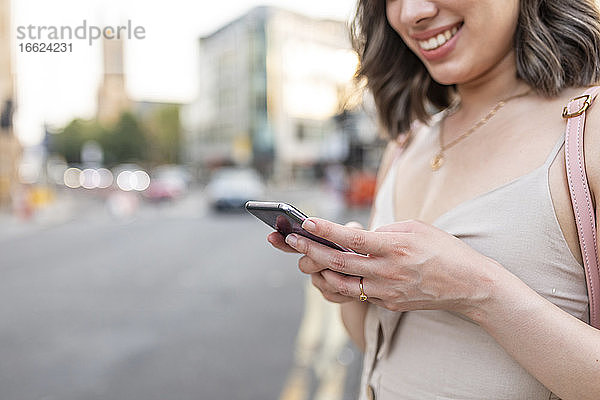 Nahaufnahme einer Frau  die in der Stadt stehend eine SMS auf ihrem Smartphone schreibt