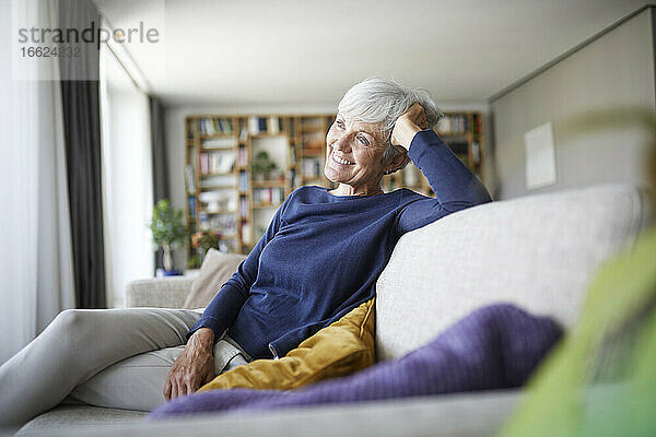 Lächelnde ältere Frau mit dem Kopf in der Hand auf dem Sofa zu Hause sitzend