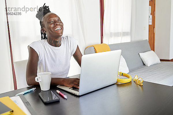 Lächelnde junge Frau bei der Arbeit am Laptop auf dem Schreibtisch im Heimbüro