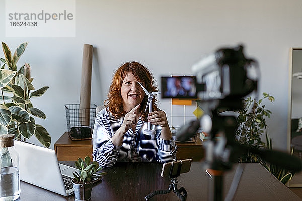 Frau macht Vlog mit Heimvideokamera  während sie zu Hause am Tisch sitzt