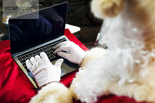 Mann im Weihnachtsmannkostüm benutzt Laptop  während er zu Hause sitzt