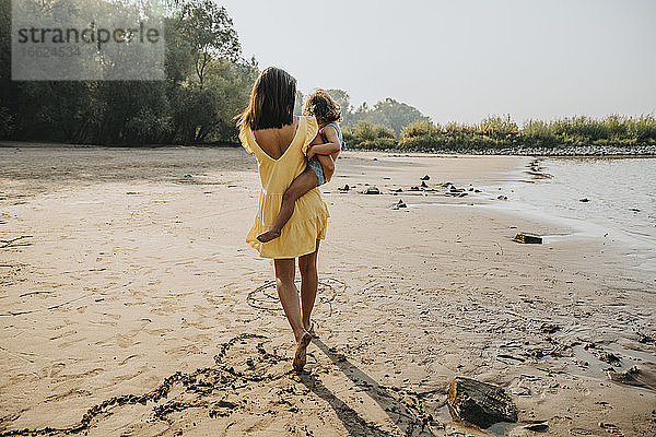 Mutter trägt ihre Tochter bei einem Spaziergang am Strand