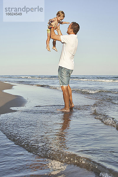 Mann holt seinen Sohn ab  während er am Strand steht