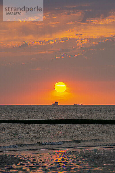 Blick auf die Sonne am orangefarbenen Himmel über dem Wattenmeer bei Sonnenuntergang