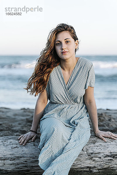 Attraktive junge Frau sitzt auf einem Baumstamm am Strand