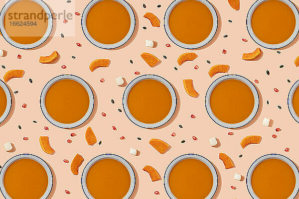 Muster von Schalen mit Kürbissuppe  umgeben von Kürbiskernen  Granatapfelkernen und Stücken von Käse und Kürbis