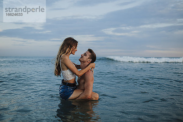 Freund trägt Freundin im Wasser stehend am Strand