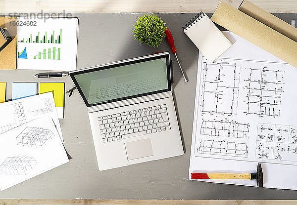 Laptop und verschiedene architektonische Werkzeuge  Entwürfe und Pläne liegen auf dem Schreibtisch im Atelier