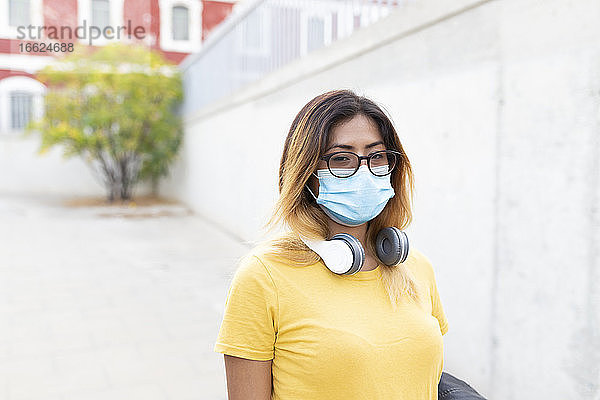 Junge Frau mit Schutzmaske und Brille an der Bushaltestelle