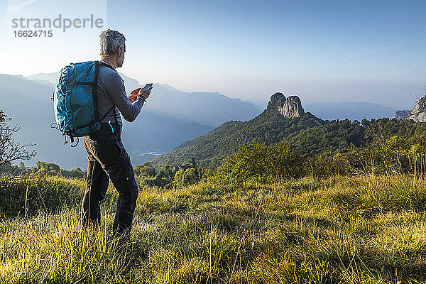 Älterer Mann benutzt sein Smartphone beim Wandern auf einem Berg bei Sonnenaufgang  Orobie  Lecco  Italien